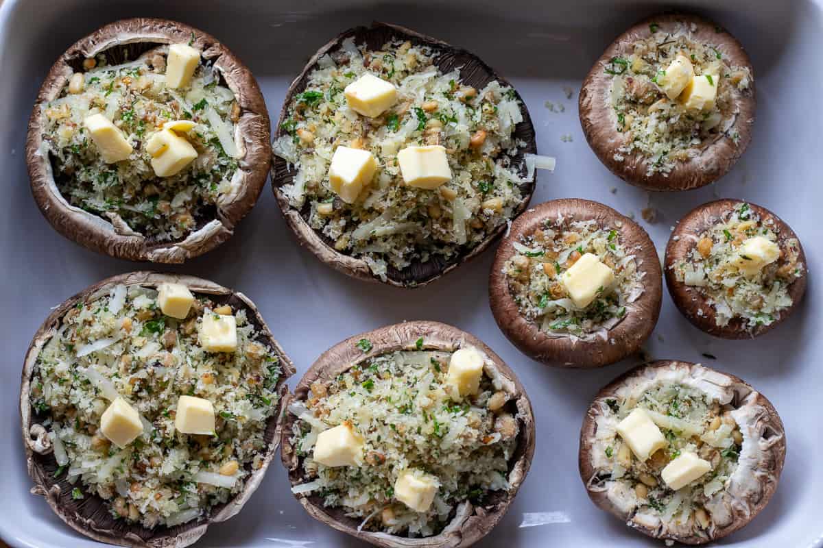 cubed butter pieces are placed on top of stuffed mushrooms