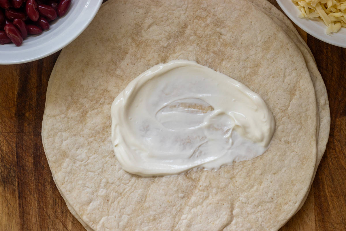 a dollop of sour cream is placed in the centre of a tortilla wrap