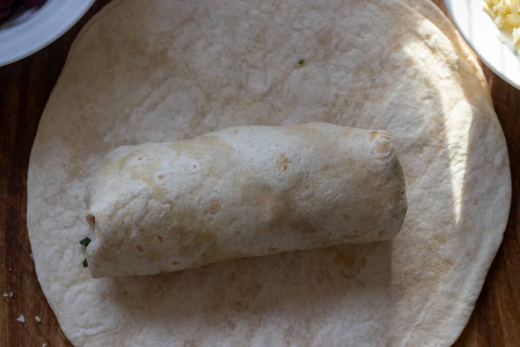 tortilla wrap is folded over beef filling to create a burrito
