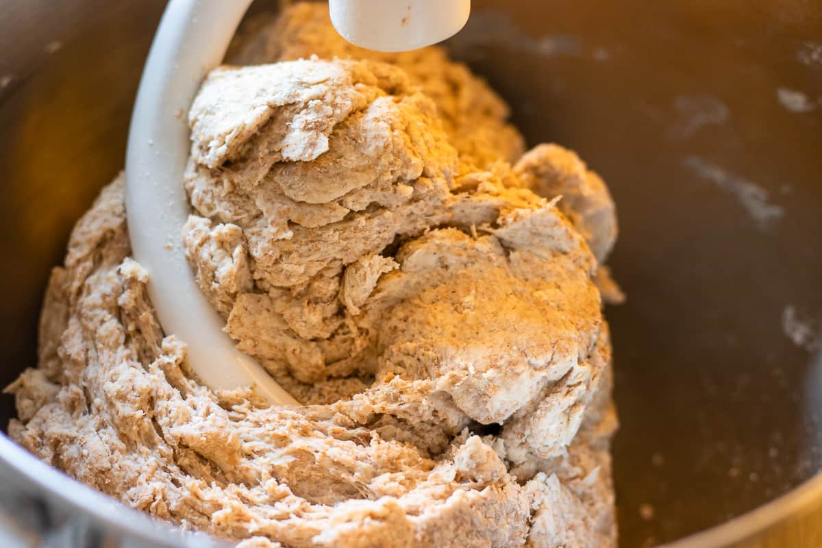 Ingredients for bread are in a bowl of a stand mixer with the hook attachment