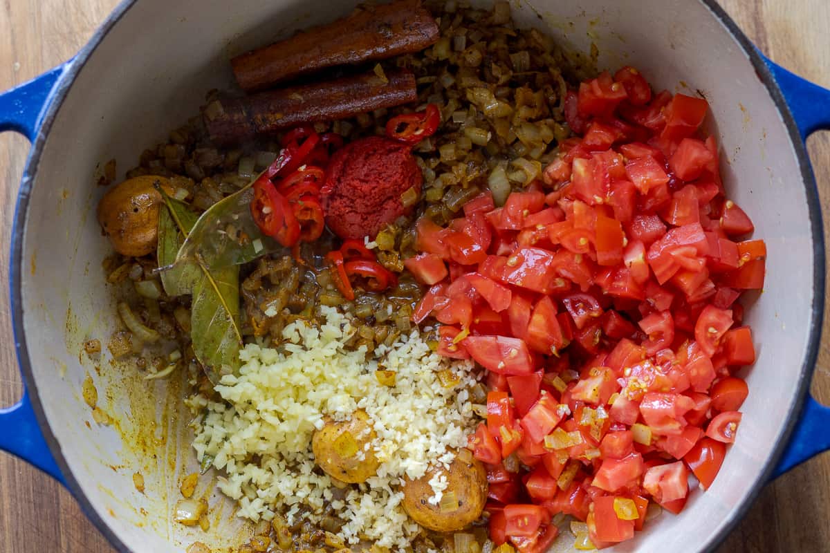 ginger, garlic, tomato paste, and tomatoes are added to the pan