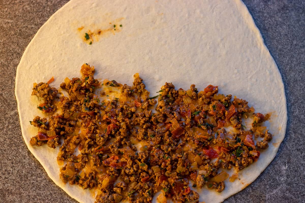 the gozleme dough is rolled out and some filling is spread on half side of the dough