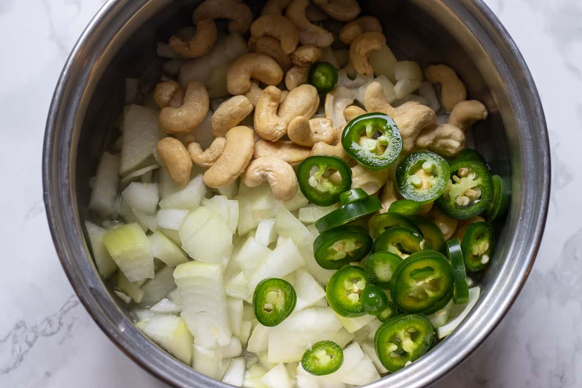 roughly chopped onions and chili are placed in a pan along with cashew nuts 
